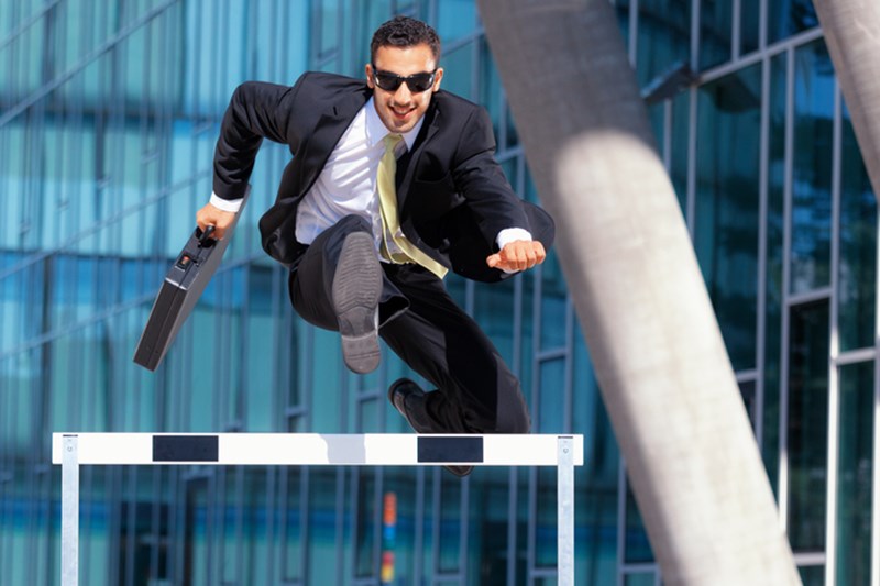 MAN IN SUIT RUNNING OVER HURDLE