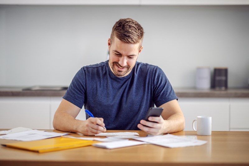 SMILING MAN SITTING AT HOME, CALCULATING BUDGET