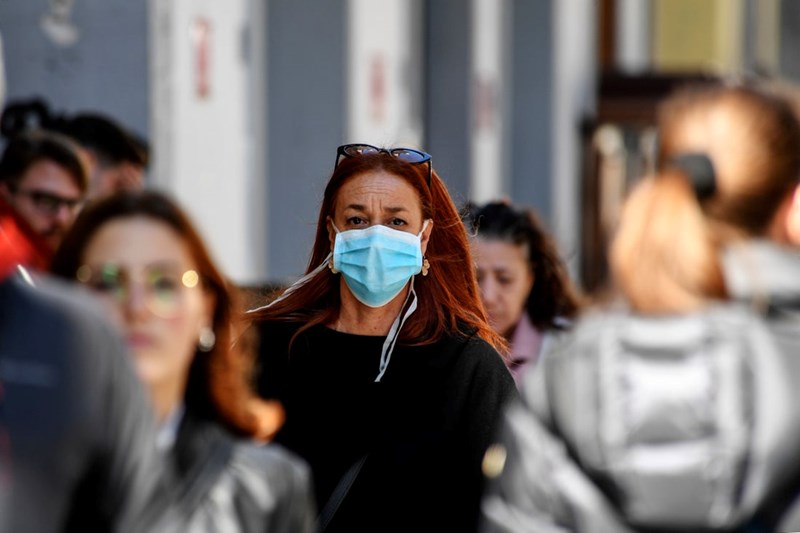 A WOMAN WALKS THROUGH THE CROWD WEARING A PROTECTIVE FACE MASK