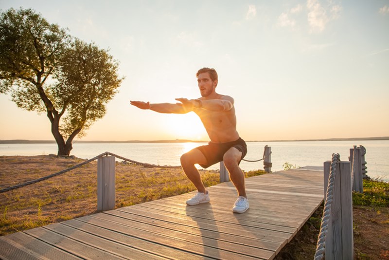 MAN DOING SQUATS ON THE BEACH