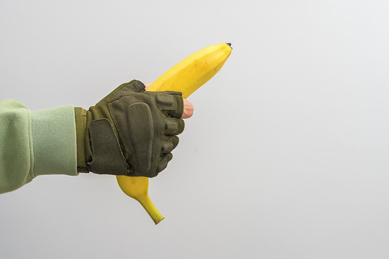 A MAN'S MILITARY HAND HOLDS A BANANA ON A GREY BACKGROUND