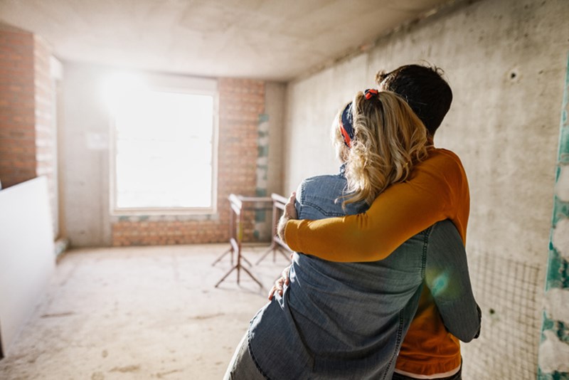 BACK VIEW OF AN EMBRACED COUPLE STANDING AT THEIR RENOVATING APARTMENT