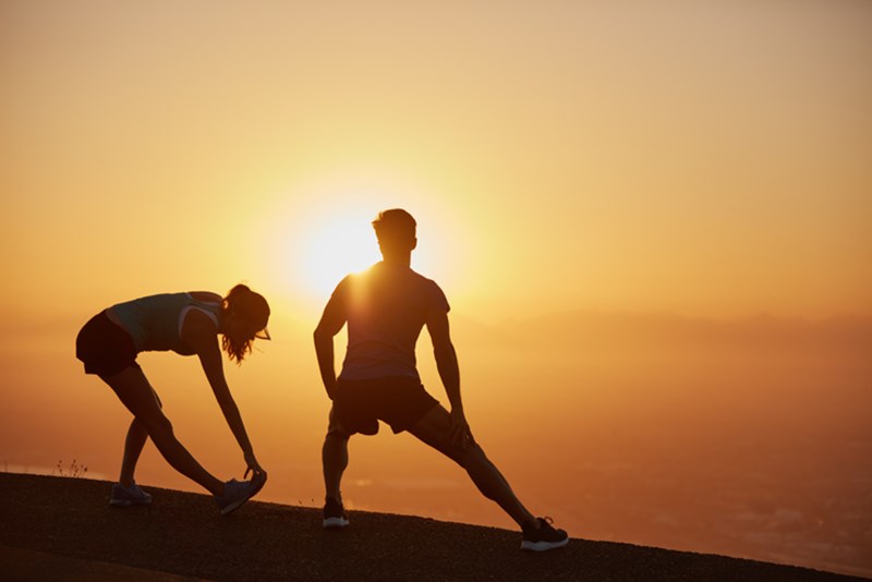 COUPLE STRETCHING BY THE SUNSET